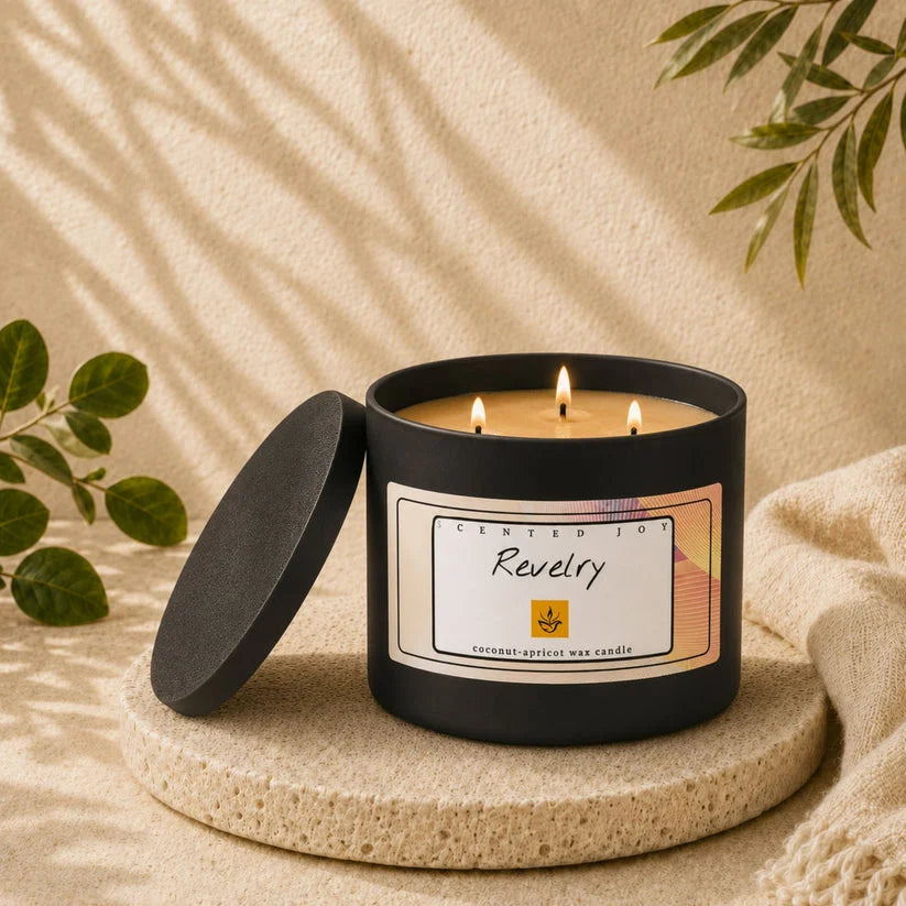 Scented Joy Revelry black 3-wick candle lit on a stone pedestal with aesthetic leaf shadows.